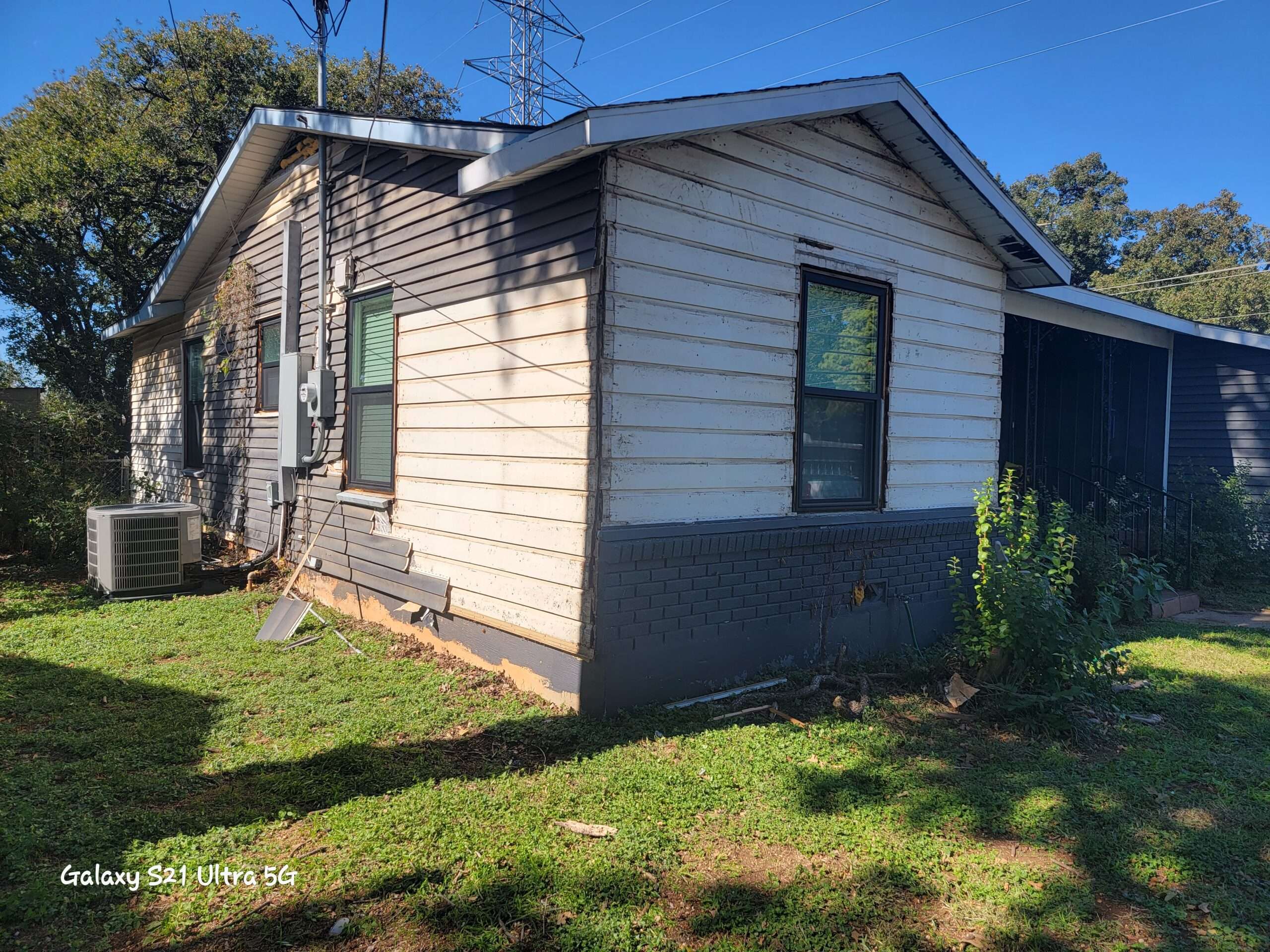 This is a small house with old, damaged vinyl siding that just got new black frame windows installed