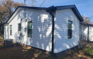 Prodigy laminated vinyl siding with board and batten accents on the front gable. White siding with black accents and new vinyl windows, viewed from the left side of the house in Hurst Texas