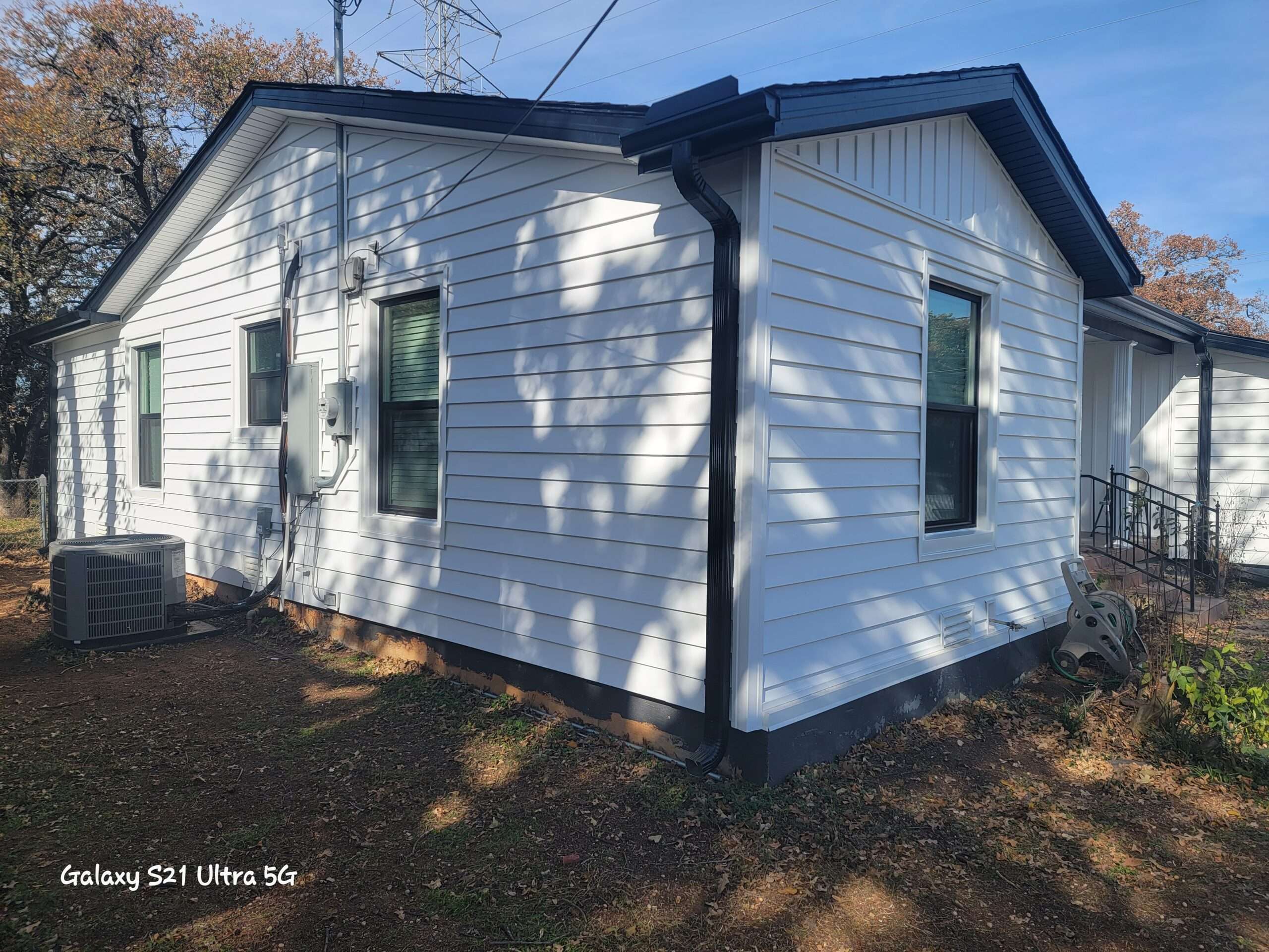 Prodigy laminated vinyl siding with board and batten accents on the front gable. White siding with black accents and new vinyl windows, viewed from the left side of the house in Hurst Texas