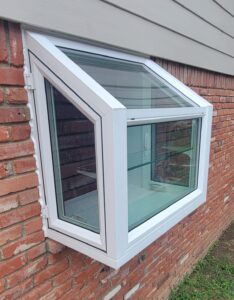 Garden style vinyl windowL ooking at the exterior of a white vinyl garden window with sloped glass on the top and casement windows on the sides to let in fresh air