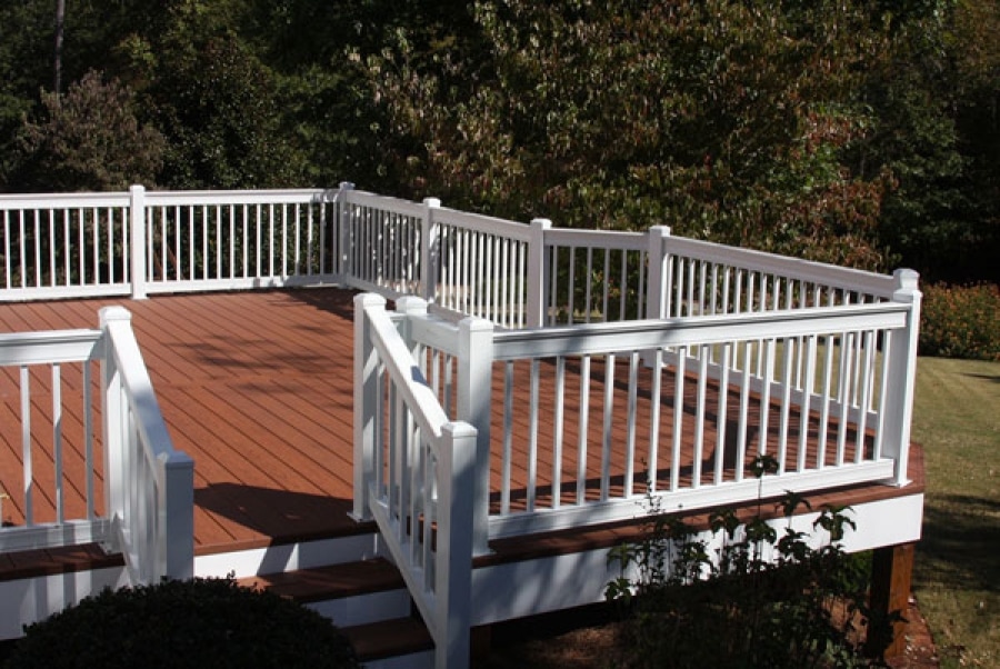 Looking at a deck that is built from Nexan LockDry Aluminum decking with a matching white aluminum railing. The deck is overlooking the back yard with green grass and pine trees in the background on a warm summer day.